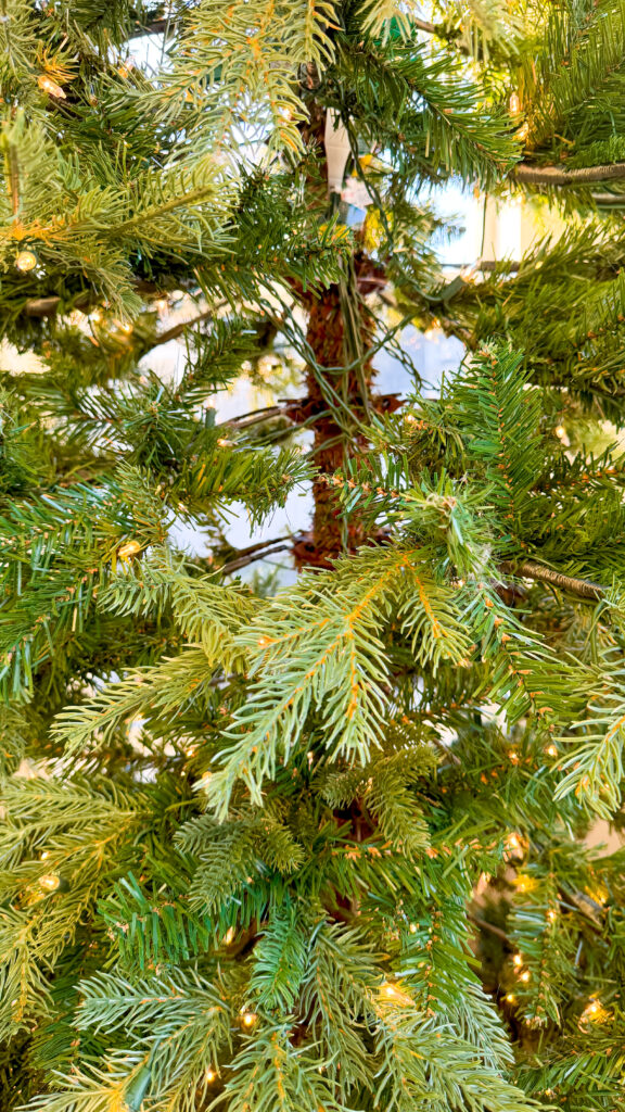 An artificial Christmas tree with large gaps and bare spots. There are few branches and pine needles in the bare spot and gaps in the tree which makes it easy to see the middle portion of the trunk of the tree along with exposed wires from the built-in Christmas lights on this particular Christmas tree.