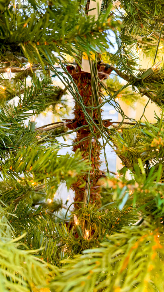 A bare gap in an artificial Christmas tree with few branches or pine needles. The middle section of the trunk of the tree is exposed along with several wires from the built-in Christmas tree lights on this particular Christmas tree, which looks unsightly.